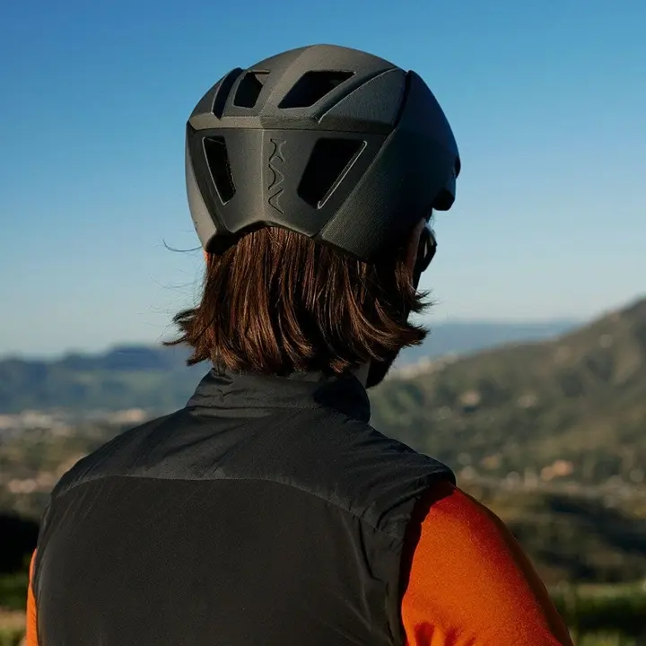 Um homem de costas com roupas de ciclista está usando um capacete preto com alguns vazados impresso em 3D.